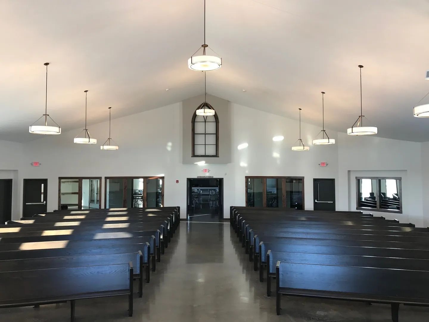Interior of a church sanctuary with rows of pews, a peaked ceiling, and several hanging lights.
