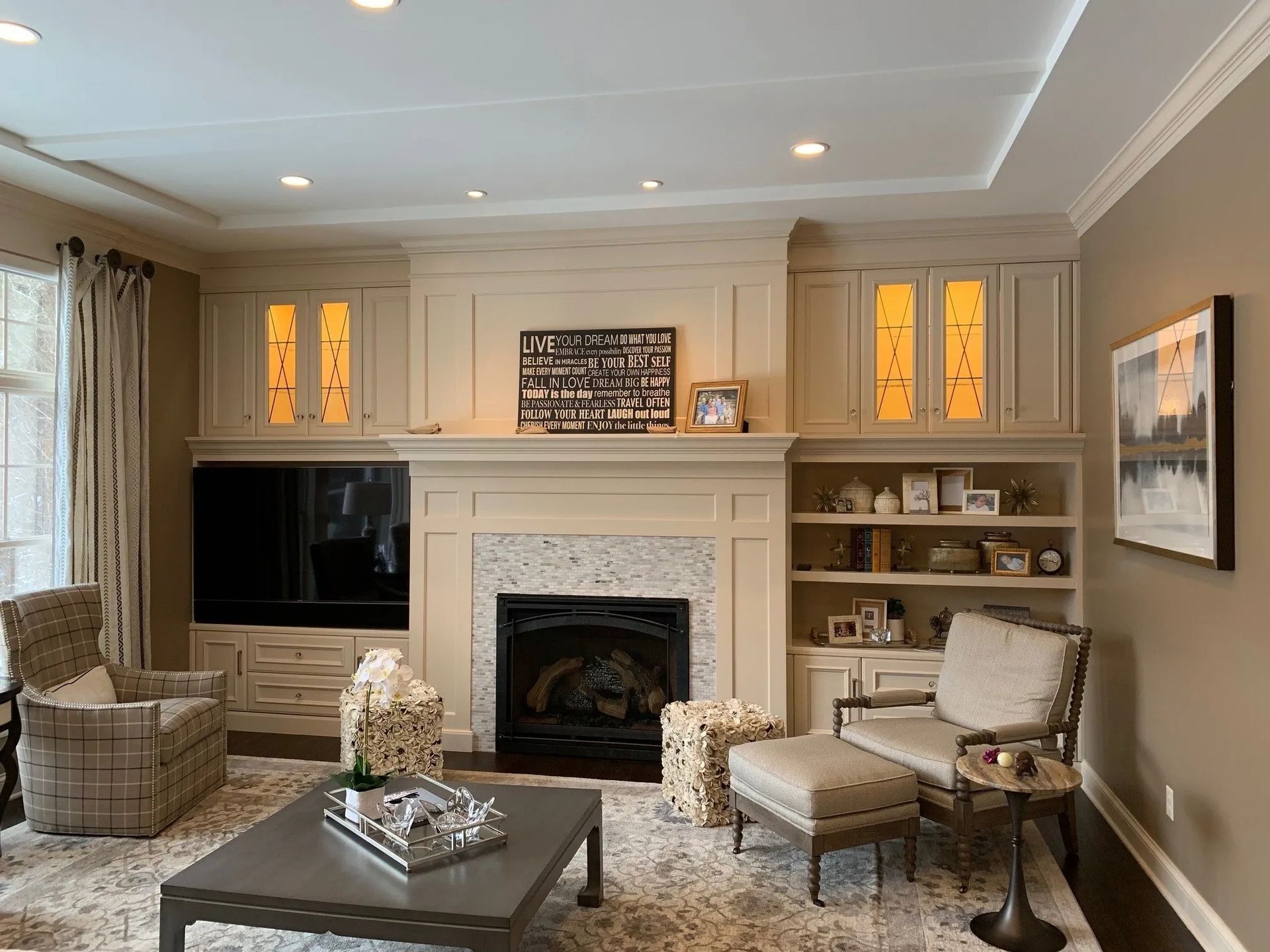 Living room with fireplace, built-in cabinets, armchair, ottoman, and coffee table.