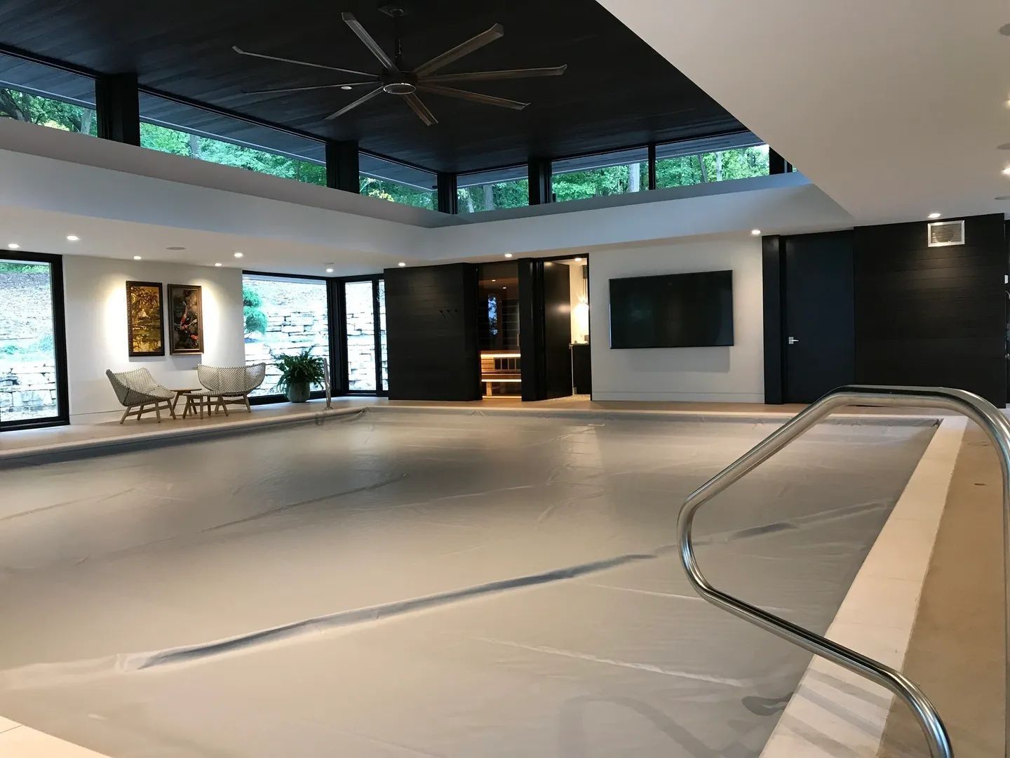 Indoor pool with closed cover. Room has large windows, ceiling fan, and modern decor.