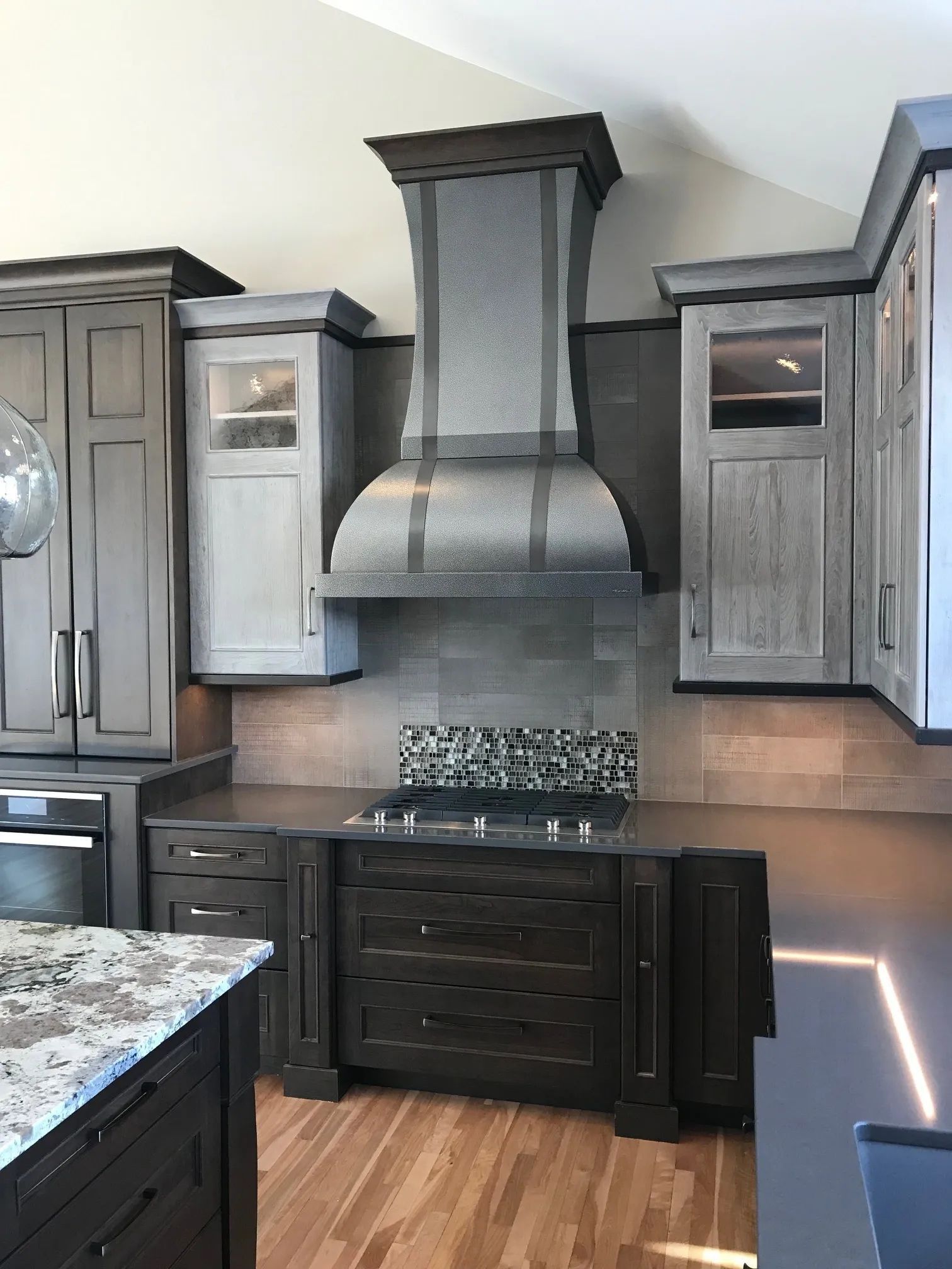 Kitchen with gray cabinets, dark island, stainless steel range hood, and wooden floor.