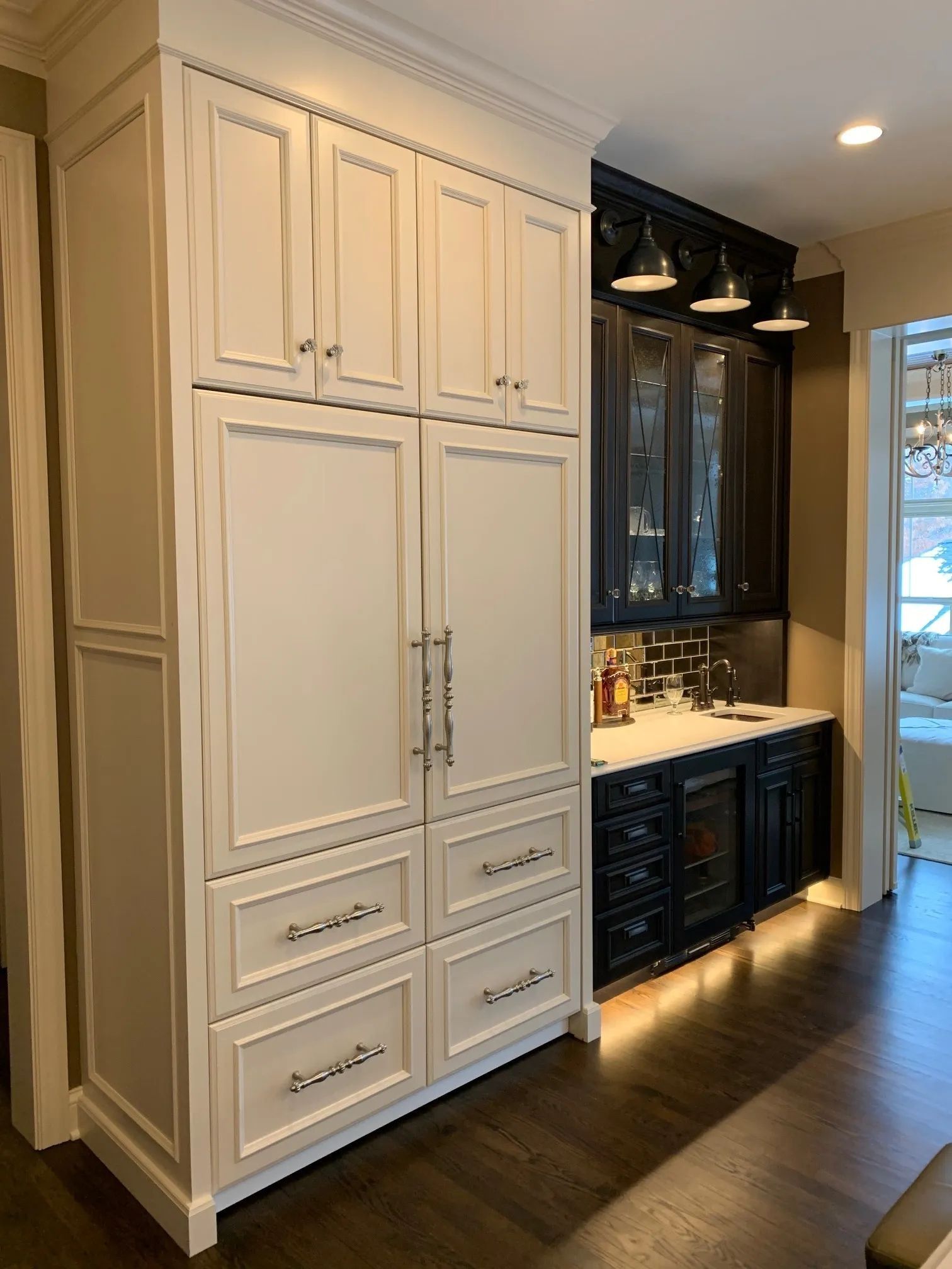 White built-in cabinetry with a refrigerator, drawers, and upper cabinets, adjacent to a dark bar area with a countertop.