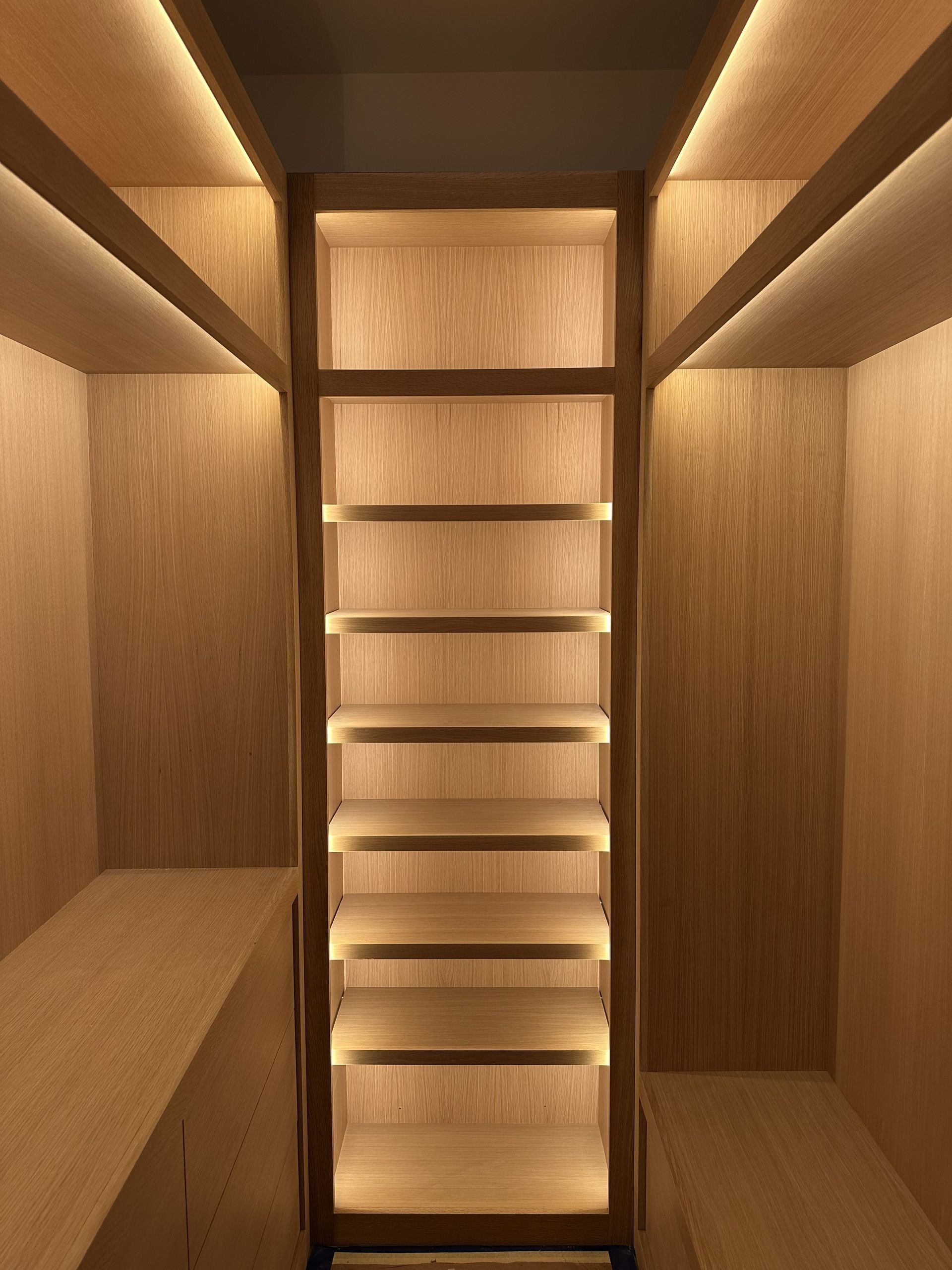 Wooden built-in shelving unit with integrated lighting. Interior view of a closet or storage space.