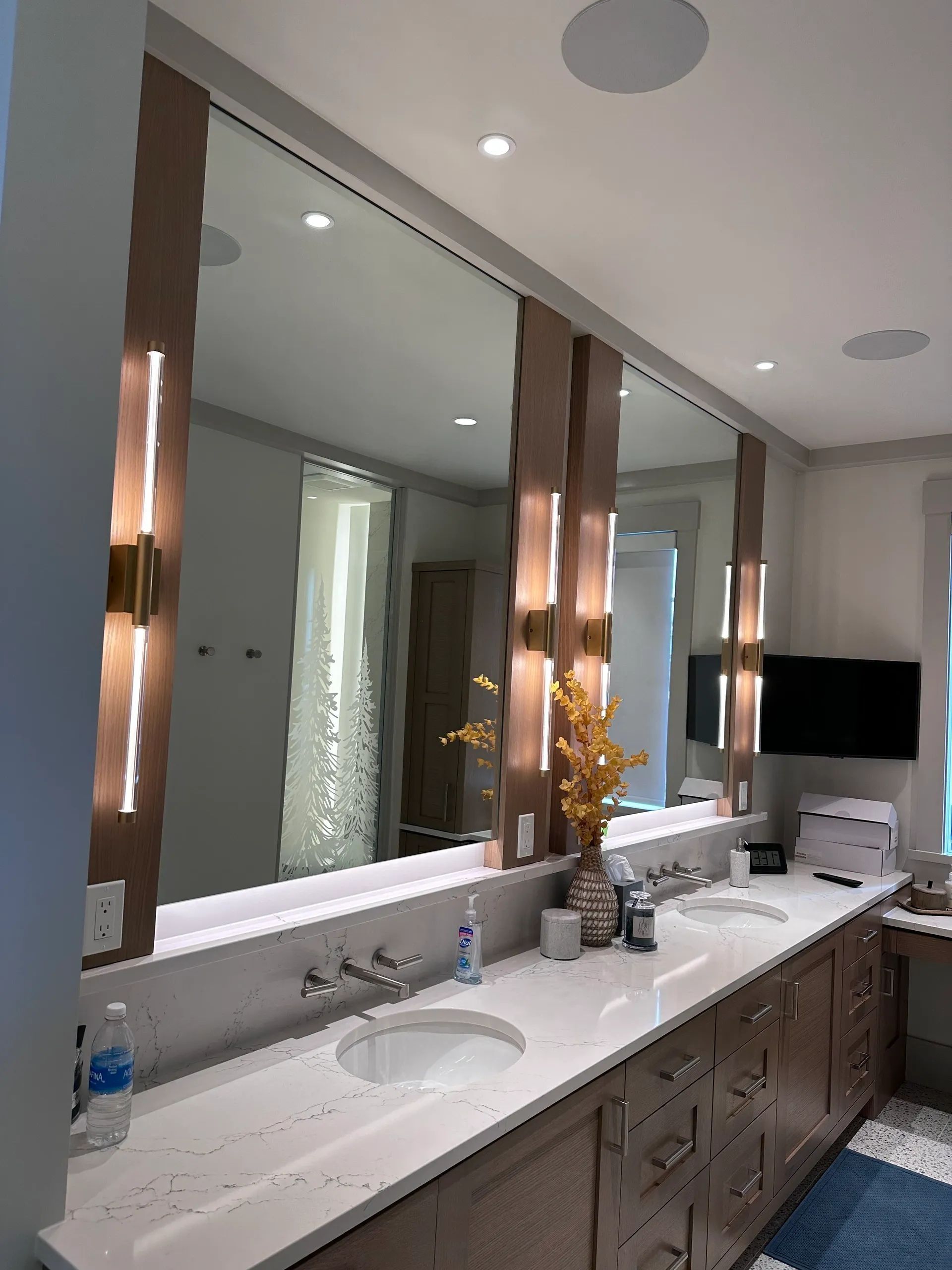 Bathroom with long countertop, three mirrors, and sconces.