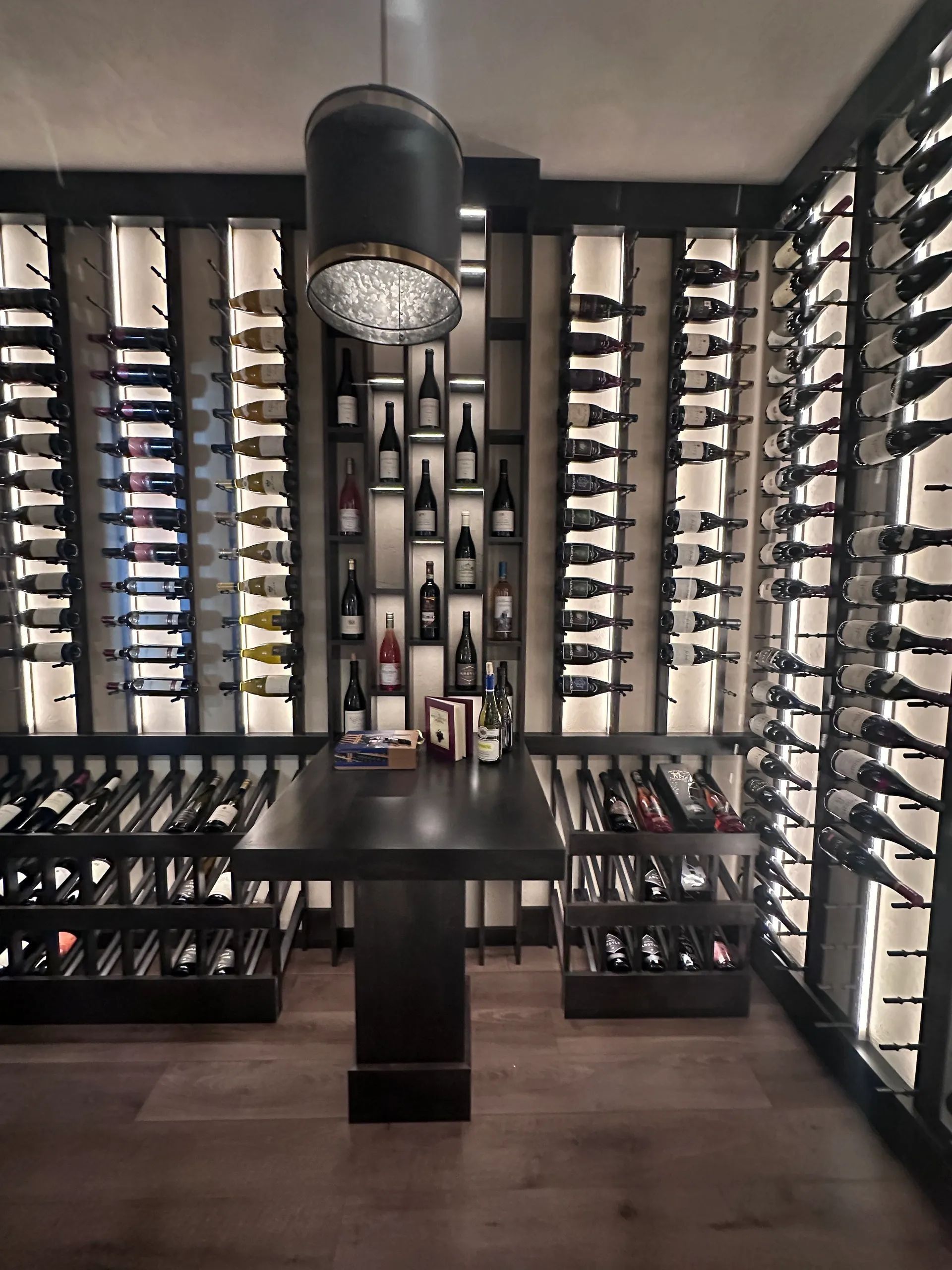 Wine cellar with dark wooden racks filled with bottles, central table, and pendant light.