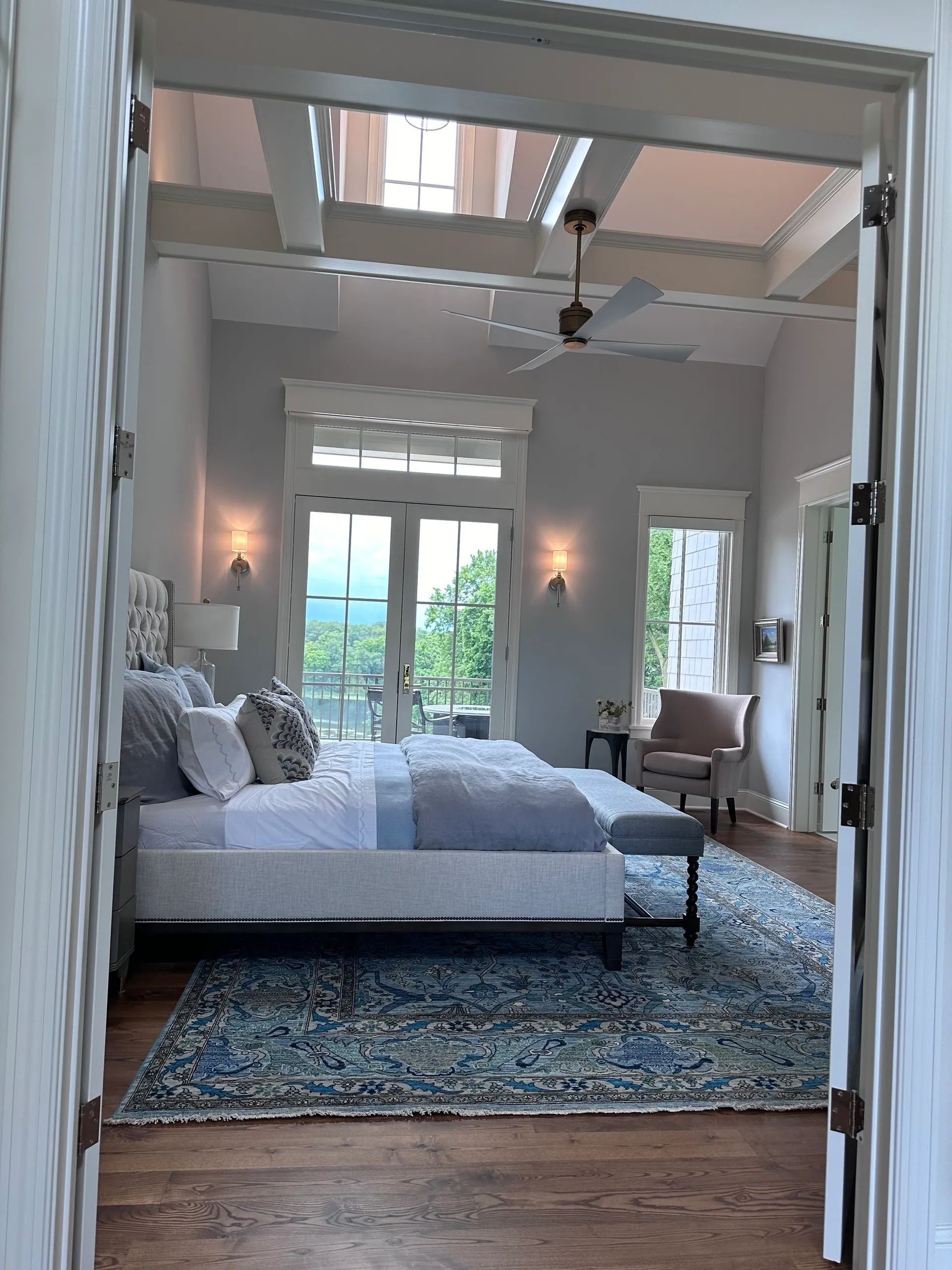 Bedroom with a bed, rug, and balcony access. Light blue and white color scheme. Ceiling fan and light fixtures.