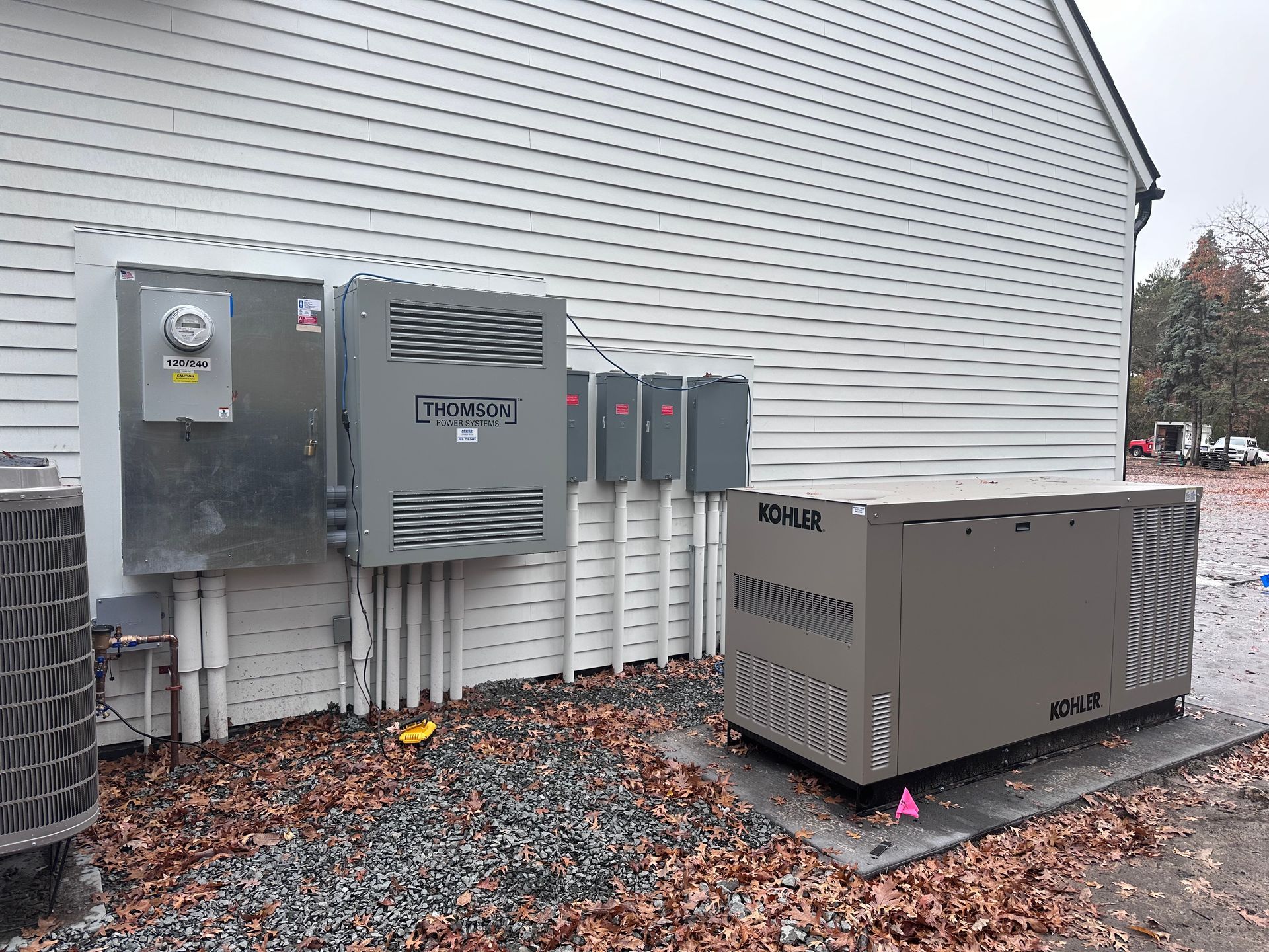 Exterior electrical equipment: generator, boxes, and conduits mounted on a house wall.
