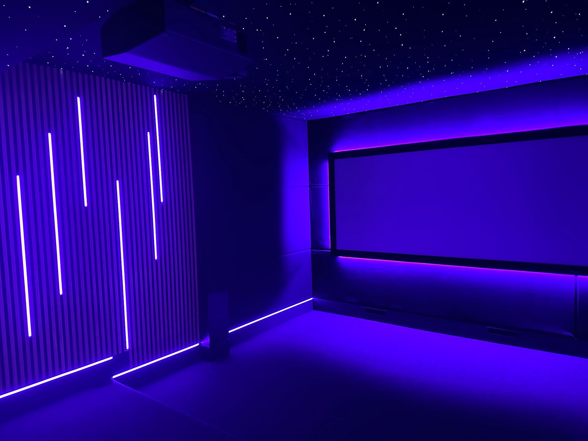 A dark room with purple LED lights, a large screen, and a starry ceiling.
