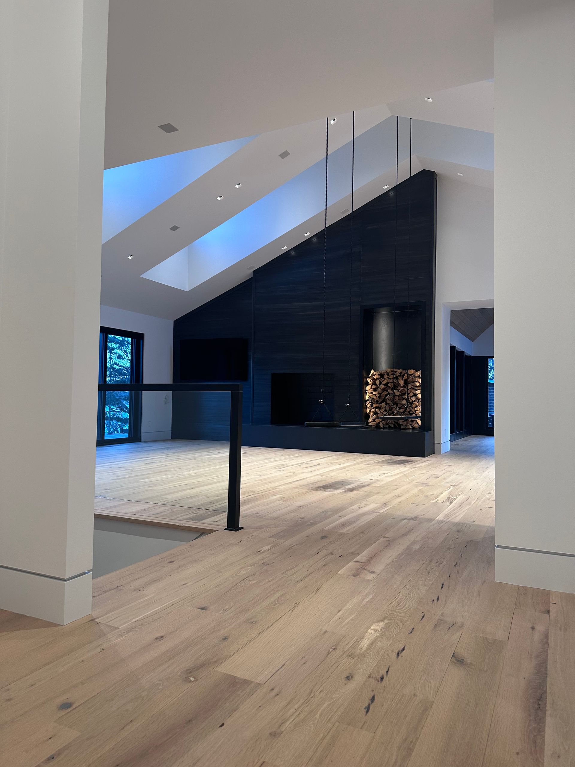 Modern living room with light wood floors, a dark fireplace, and a high, sloped ceiling with skylights.