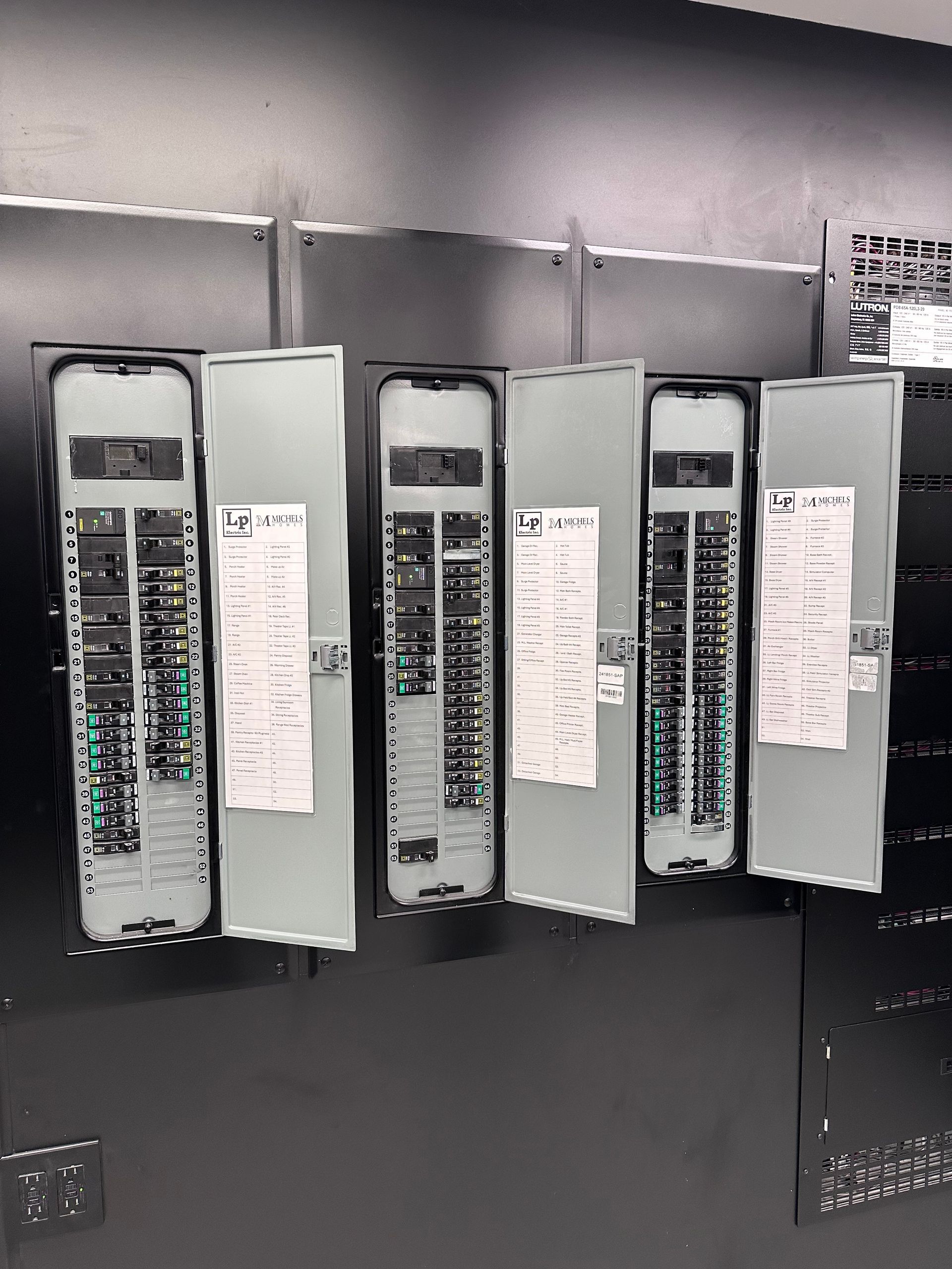 Electrical panels mounted on a dark wall. Several panels are open, revealing circuit breakers and labels.