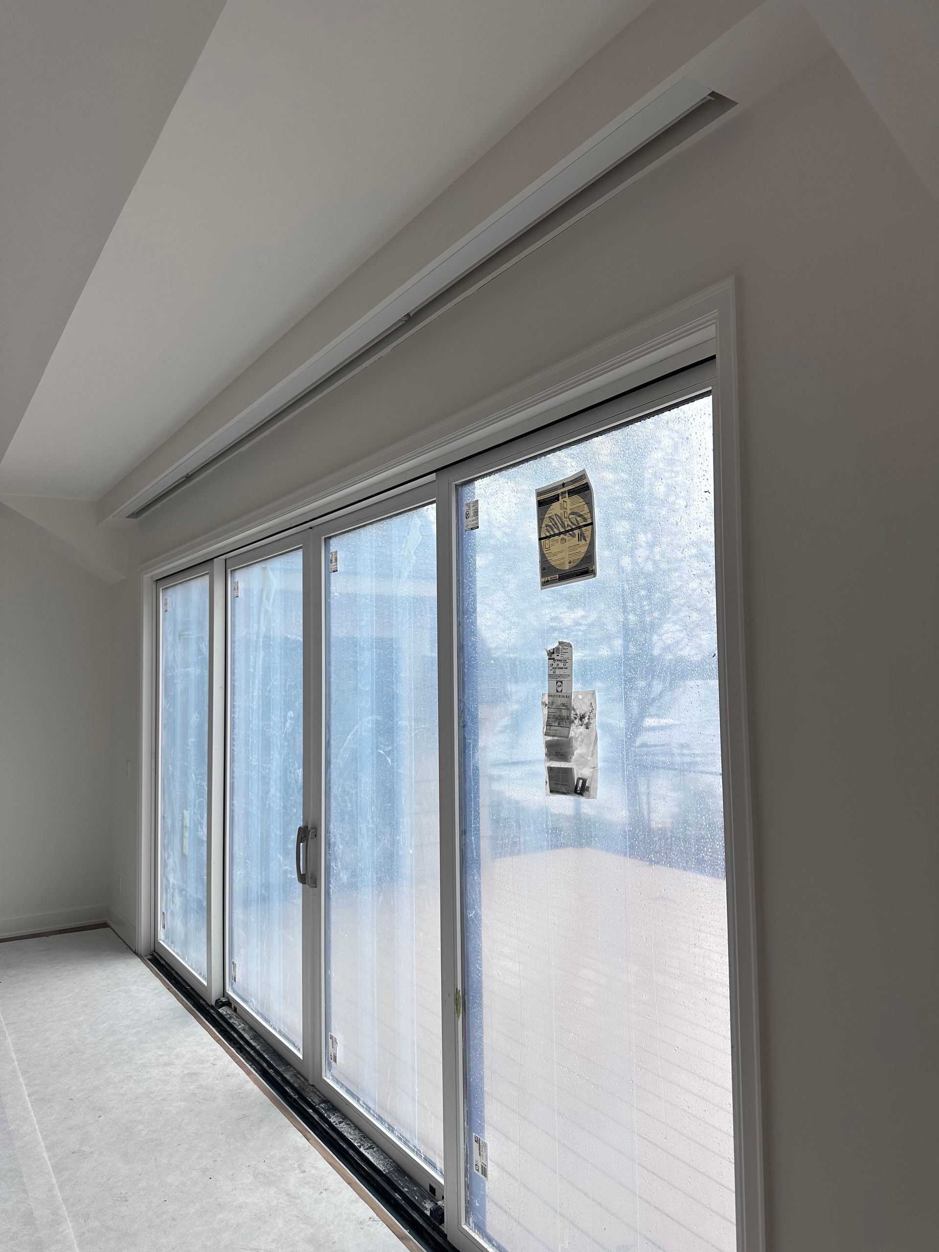 Sliding glass doors with white frame, installed, inside a room with a white wall, and a ceiling vent.