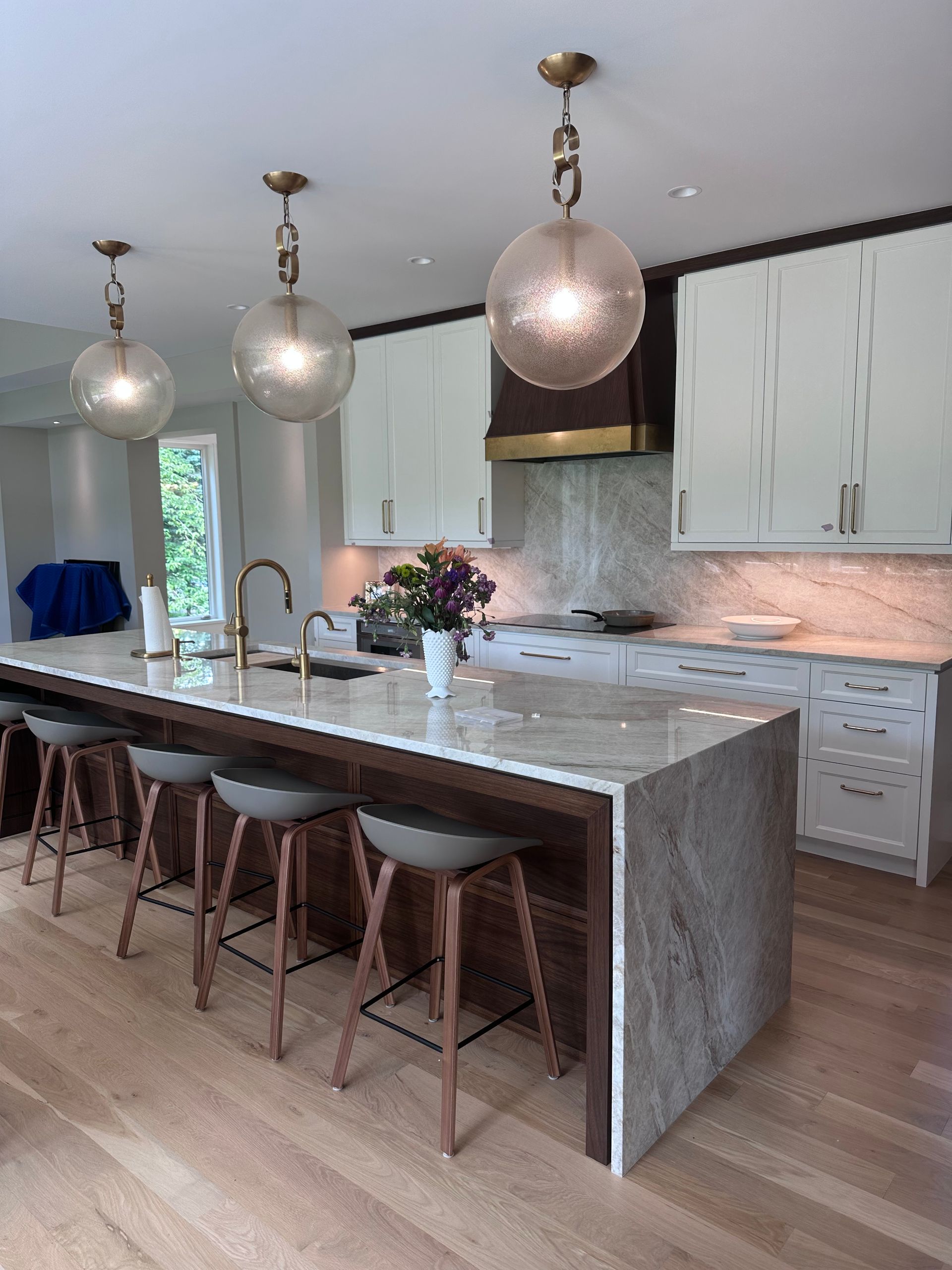 Kitchen with a large island, three pendant lights, and bar stools. White cabinets and granite countertops.