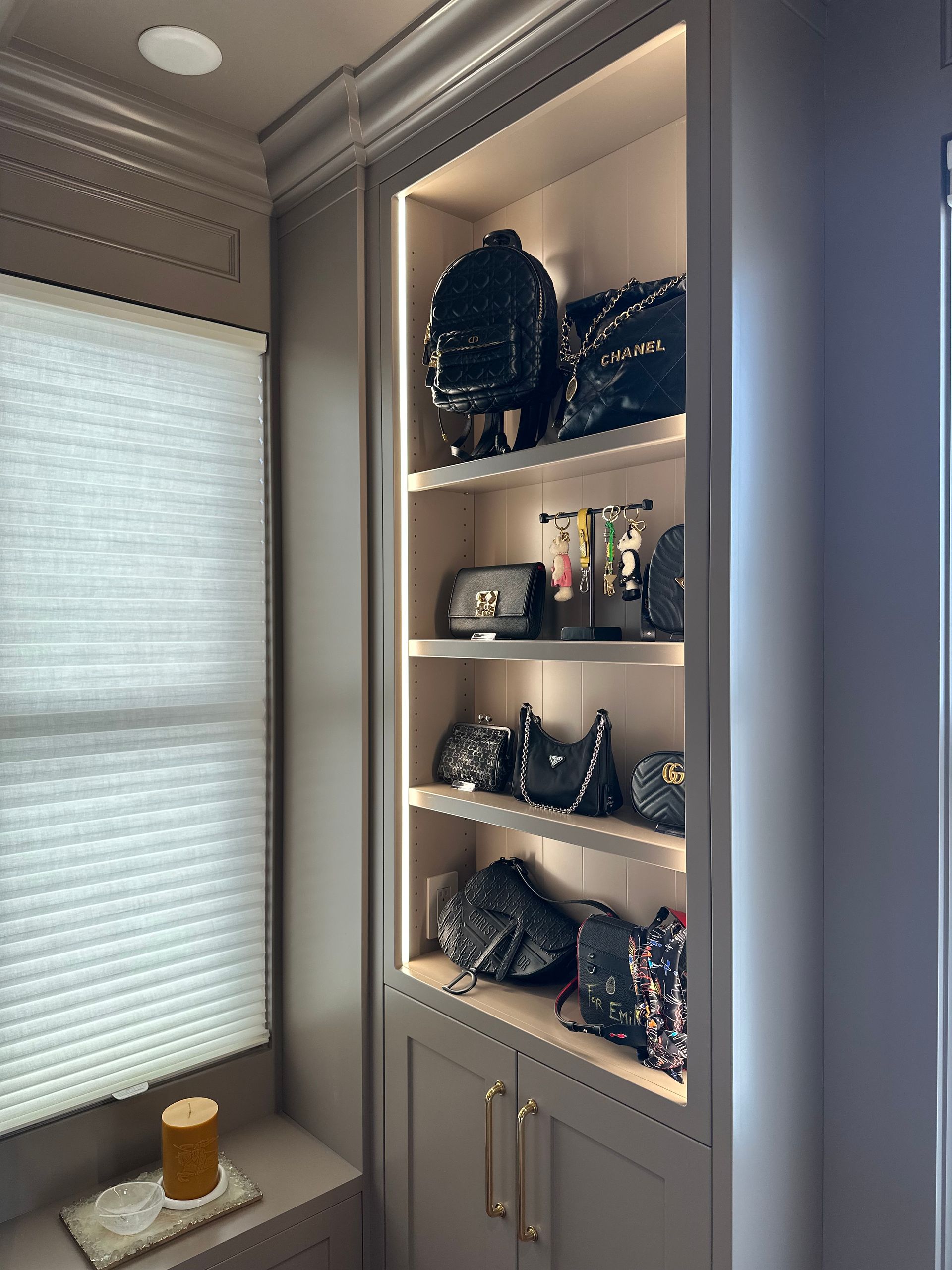 Built-in cabinet displaying black purses and a backpack, with interior lighting.
