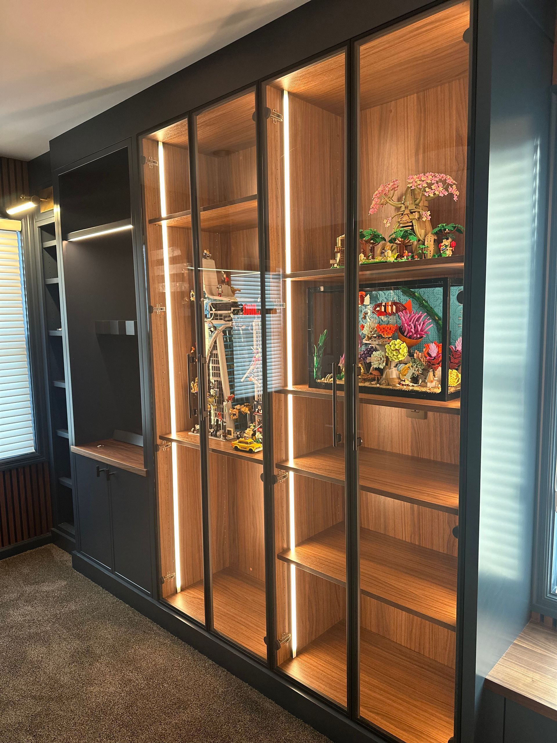 Built-in wooden cabinet with glass doors, illuminated shelving, and decorative items.