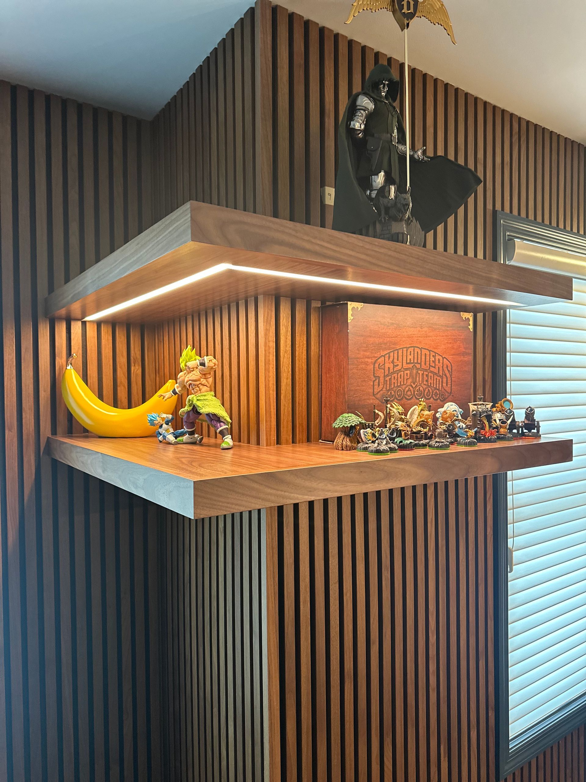Wooden shelves with figurines and a banana on wood-paneled wall; lit with LED lights.