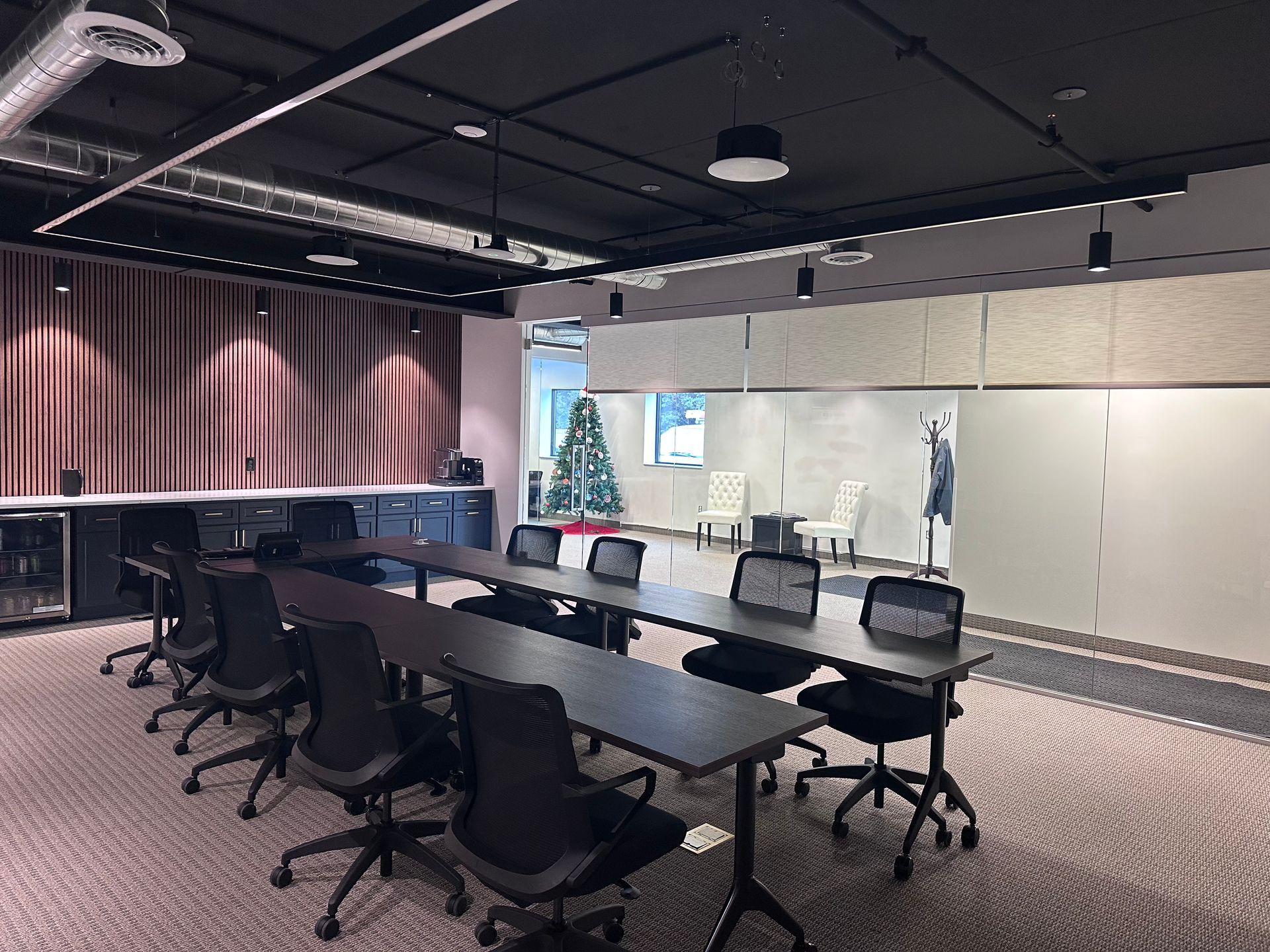 A modern conference room with a long table, black chairs, and neutral-toned walls.