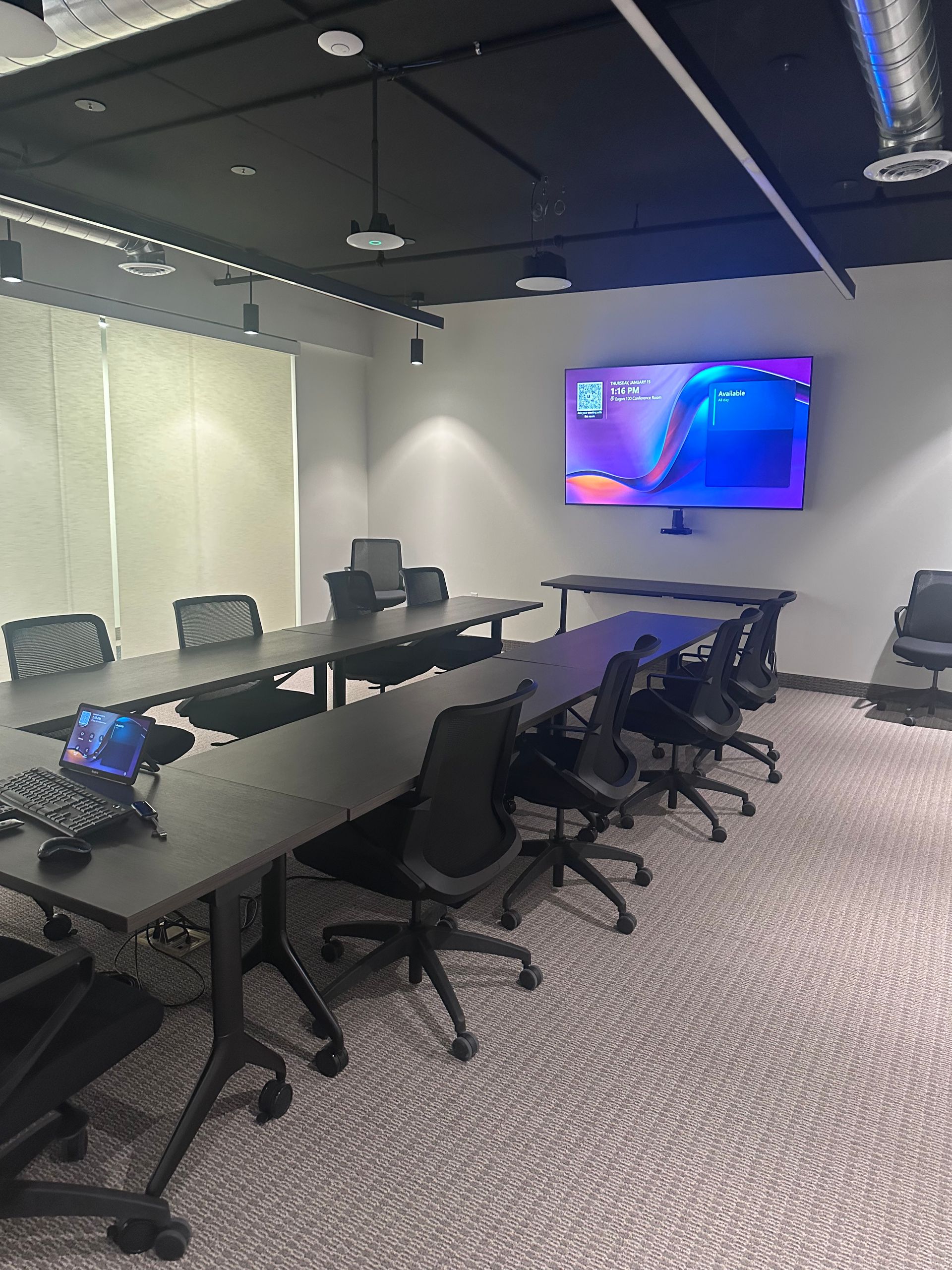 Conference room with long tables, chairs, and a large screen displaying a colorful graphic.