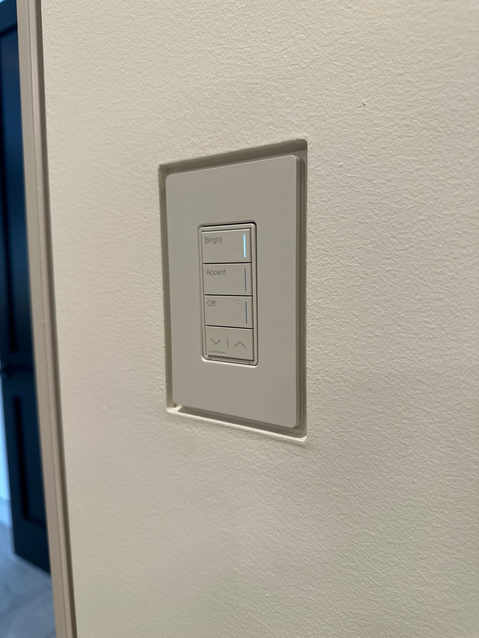 Light switches on a textured white wall. Three switches in a recessed light-colored panel. Doorway visible in the background.