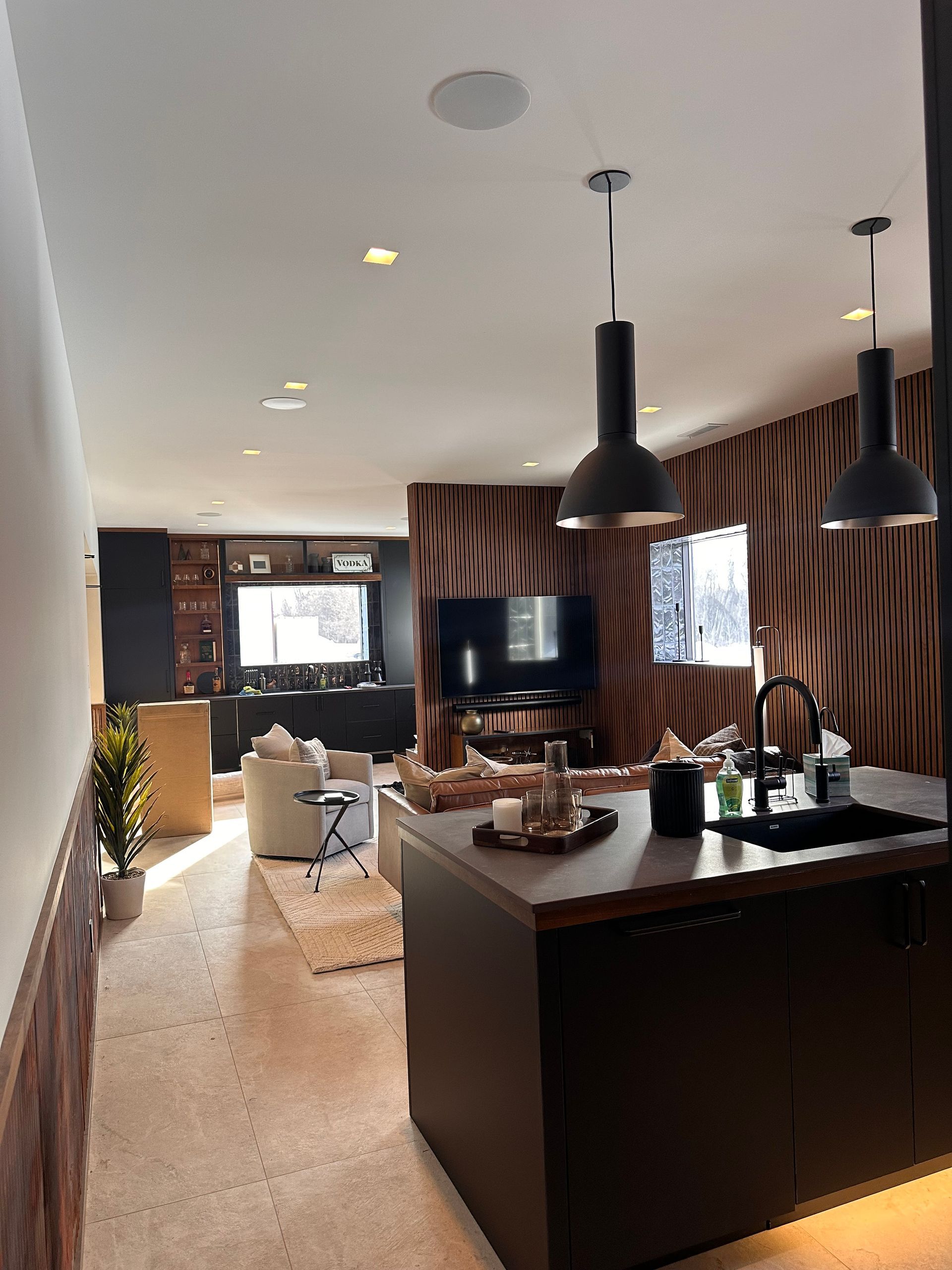 Modern kitchen and living area with island, dark cabinets, pendant lights, and tiger print wall.