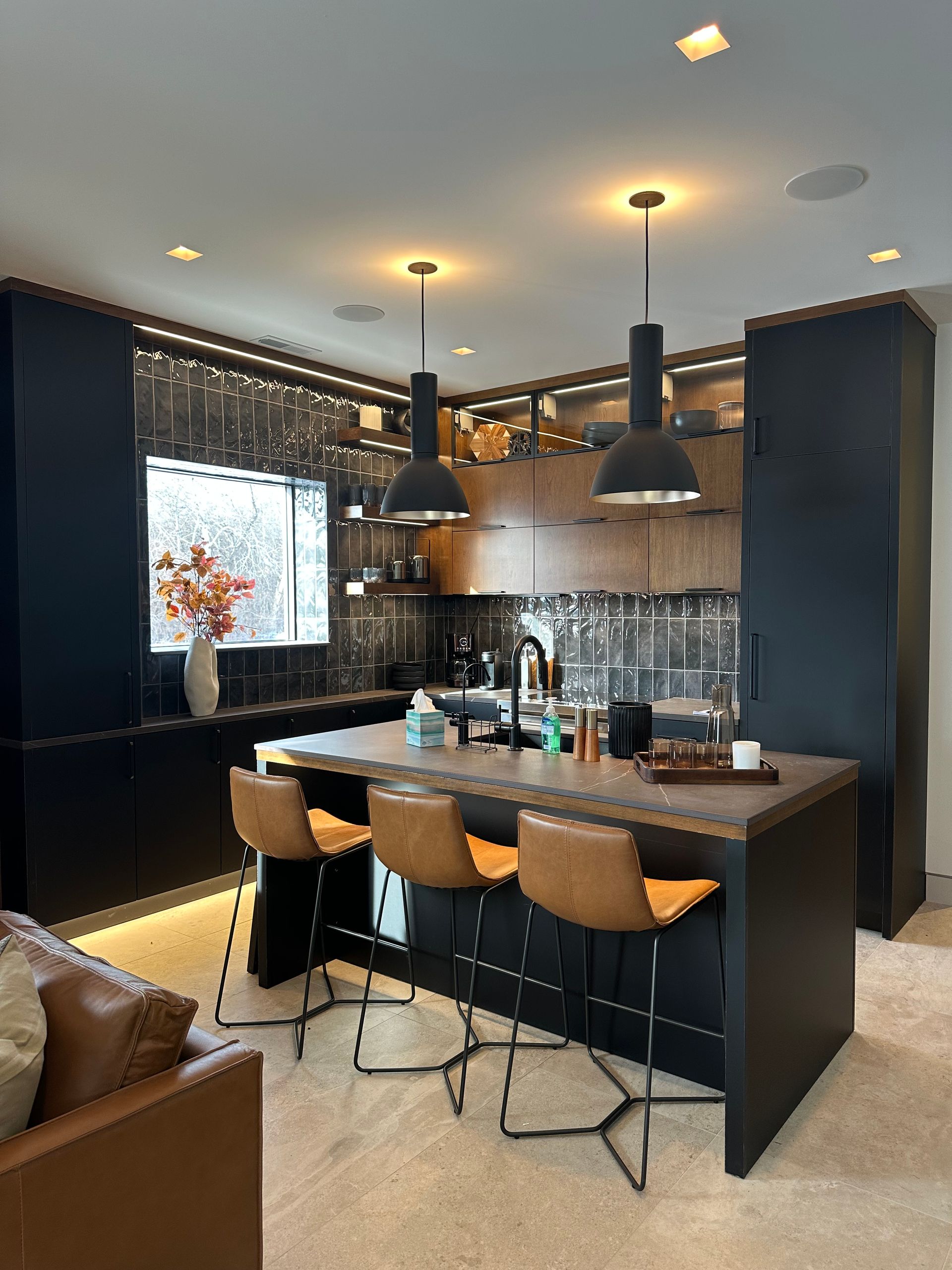 Modern kitchen with a black island, bar stools, and overhead pendant lights.