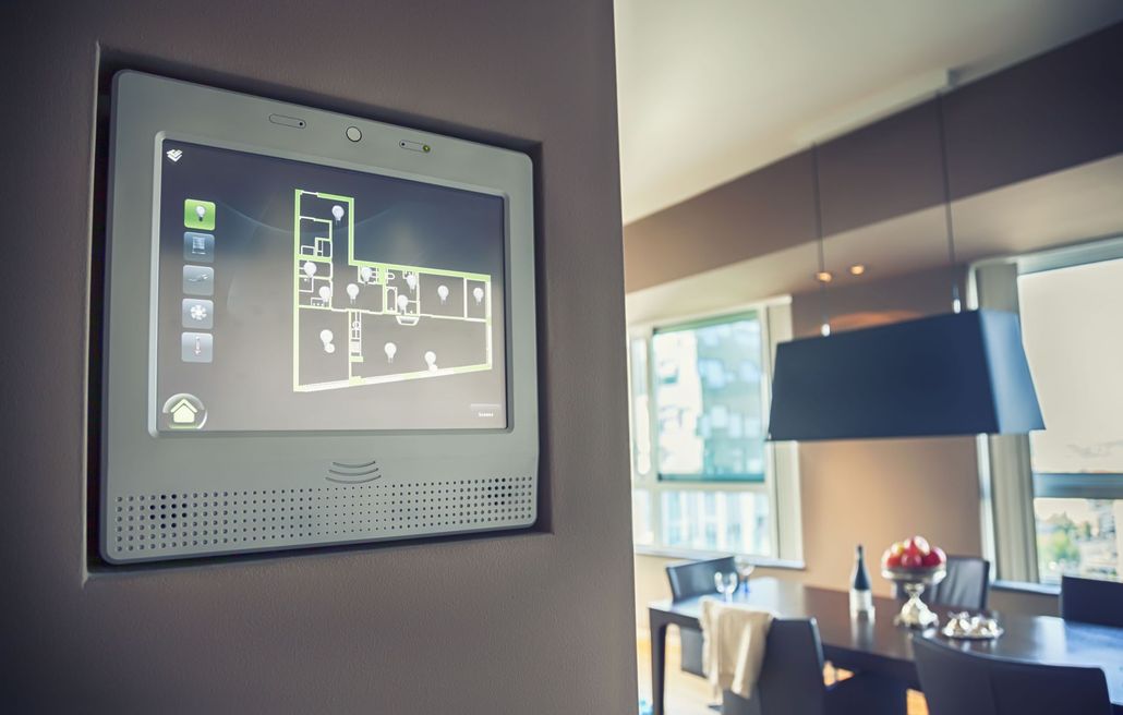 Wall-mounted smart home control panel displaying a floor plan in a modern dining room.