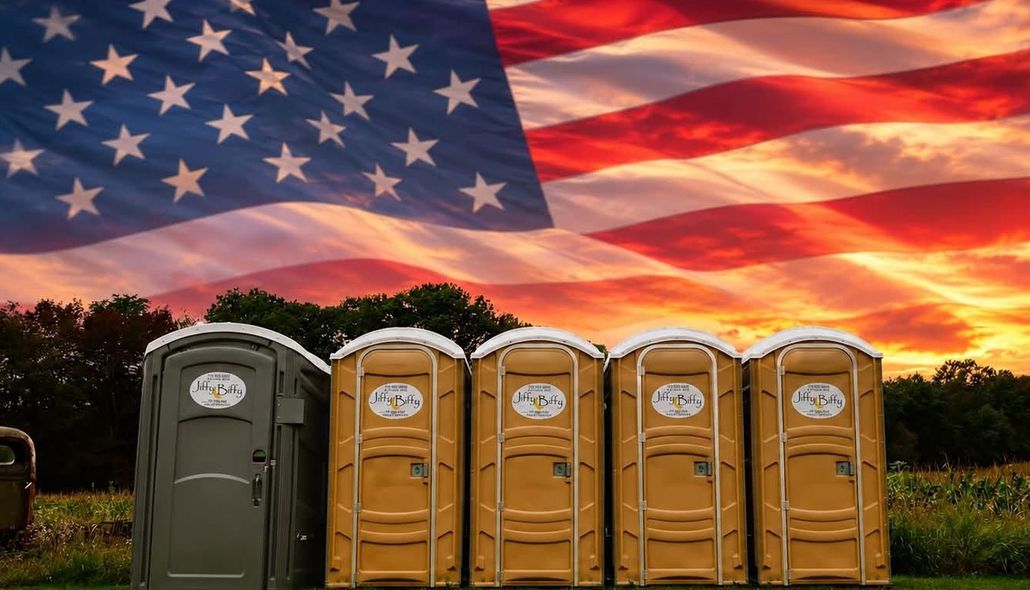 Portable toilets in front of a large American flag at sunset