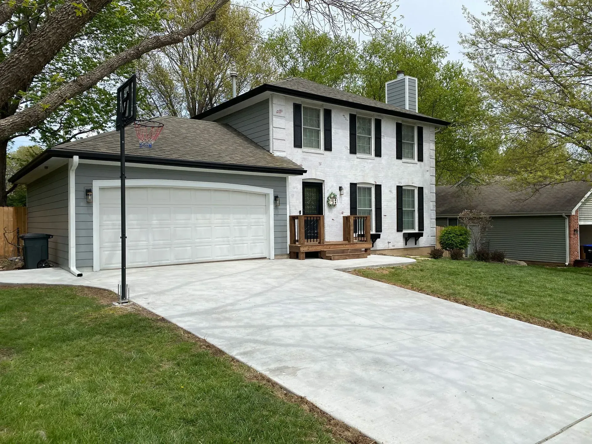 A two-story white house with dark shutters and an attached gray garage, featuring a newly paved concrete driveway.