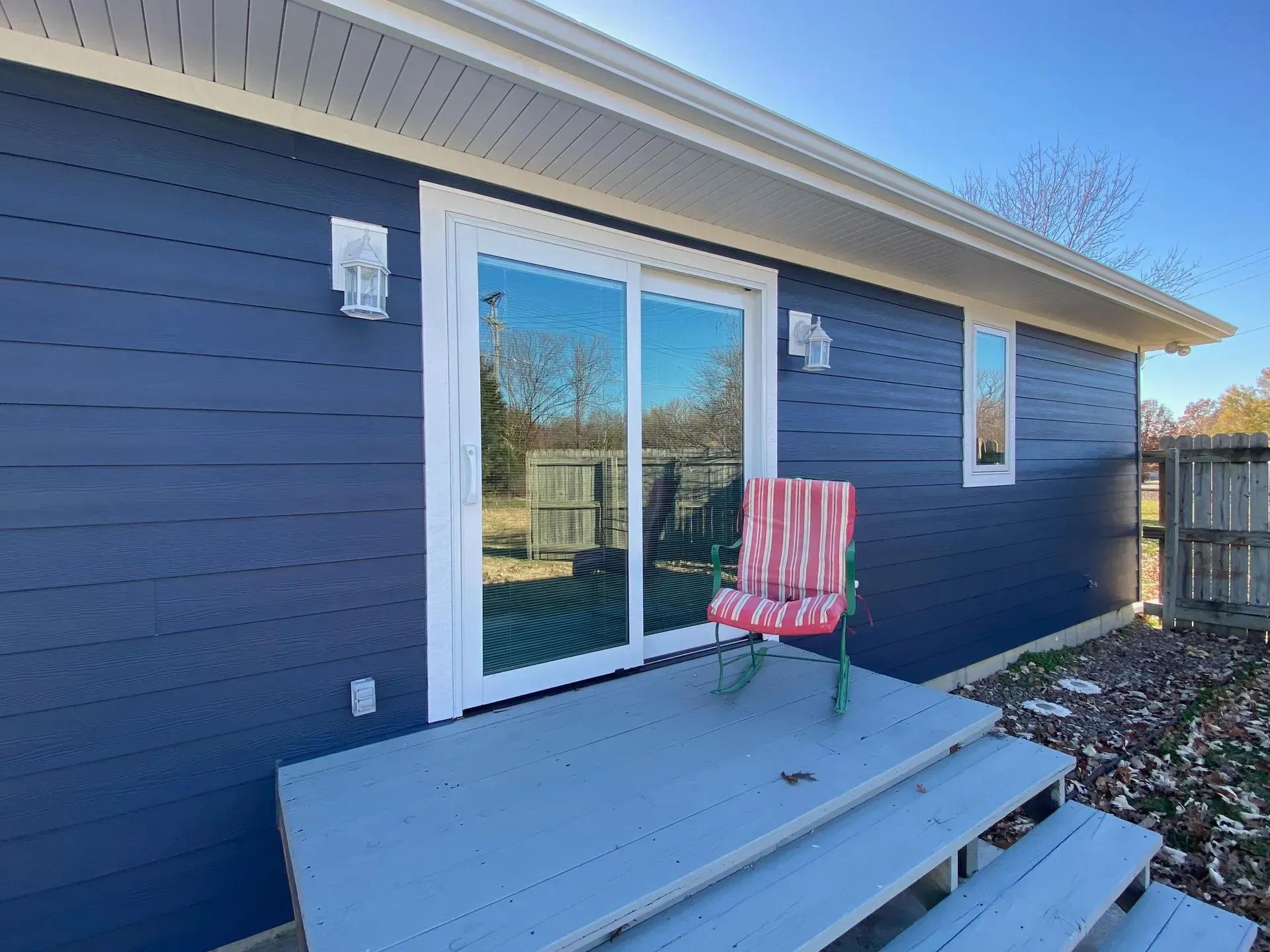 A blue house exterior with a sliding glass door, a wooden porch with steps, and a red striped rocking chair.