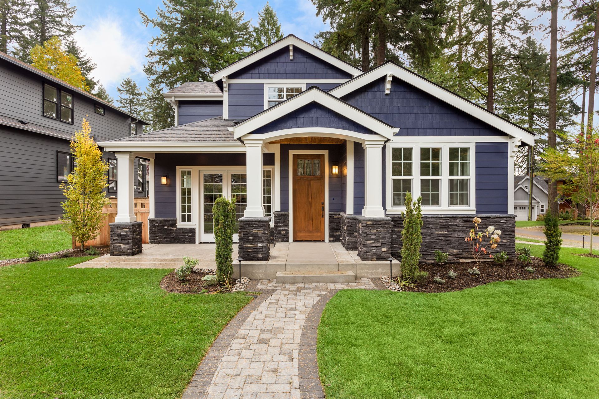A two-story blue house with a stone foundation, a wooden front door, and a stone walkway leading to a covered porch.
