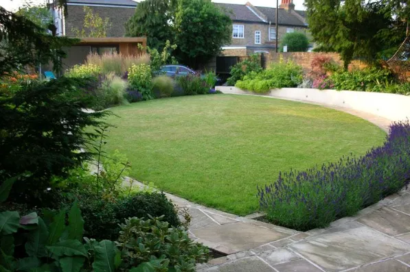 Landscaped backyard with a green lawn, curved stone path, and purple flower border