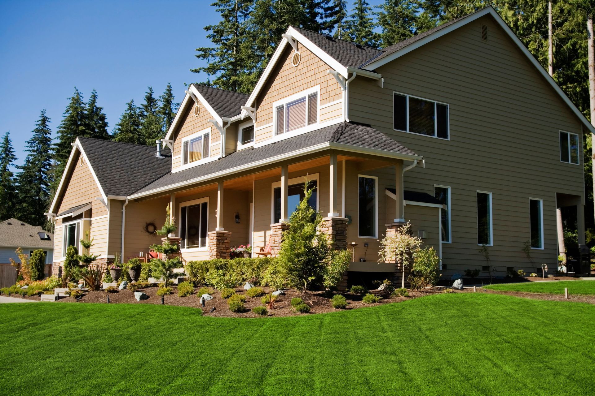 Large beige house with a front porch and green lawn under a sunny sky