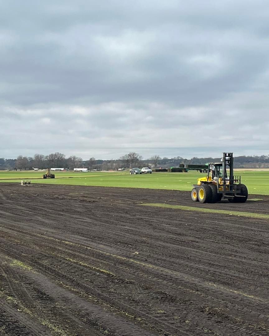 Yellow construction vehicle on a dirt field under a cloudy sky, with open grassland in the background