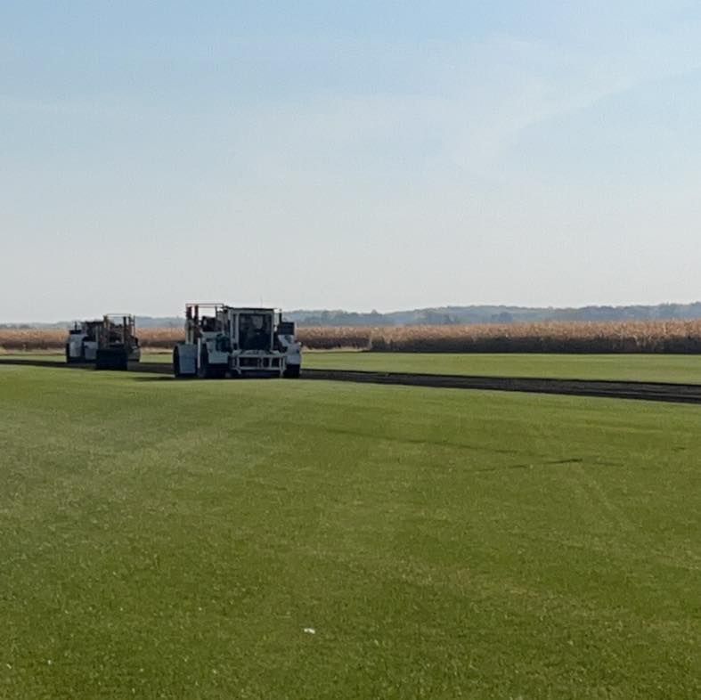 Two farm machines working on a green field under a clear sky