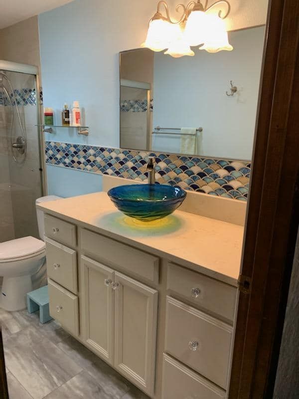 A bathroom with a sink, toilet, mirror and shower.
