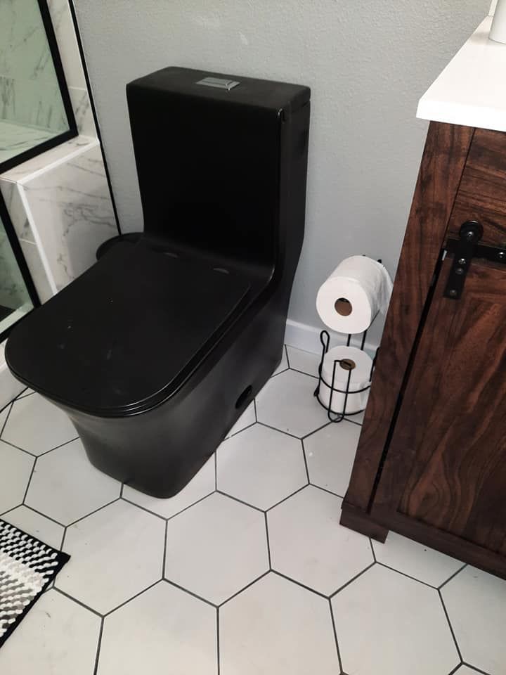 A black toilet is in a bathroom next to a paper towel holder.