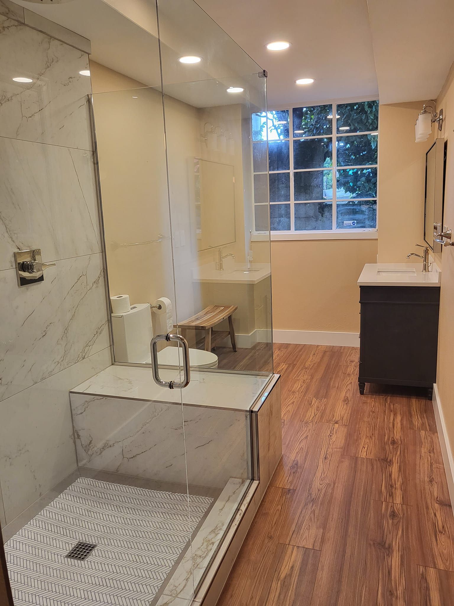 A bathroom with a walk in shower, sink, and window.