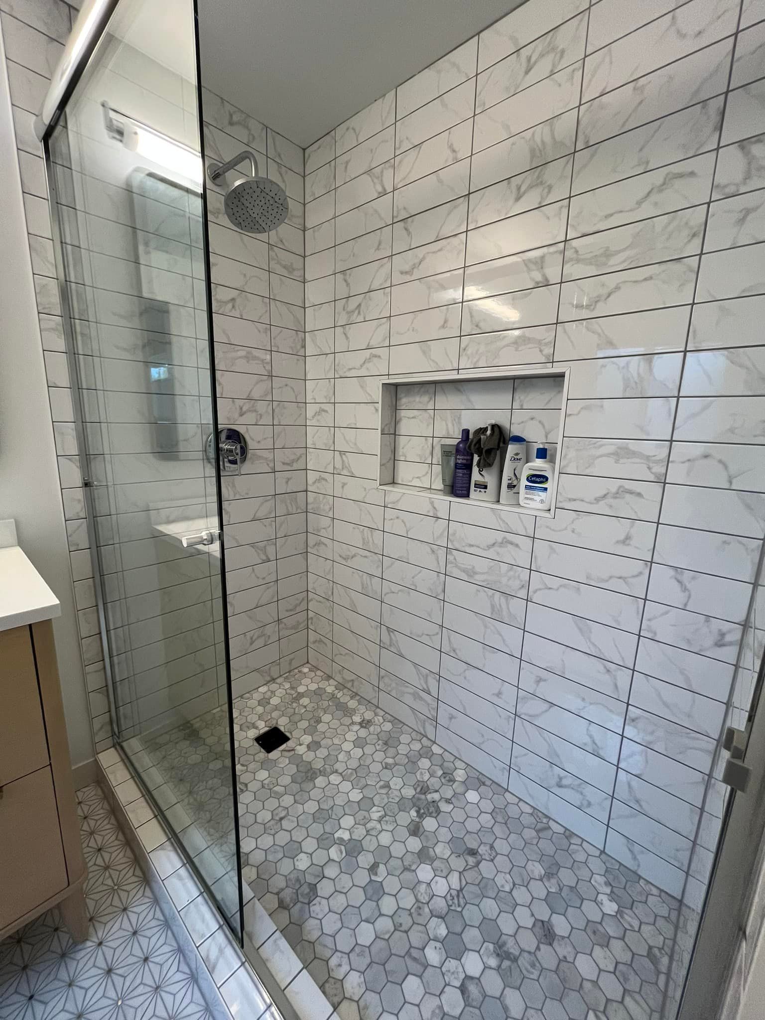 A bathroom with white tiles and a walk in shower with a glass door.