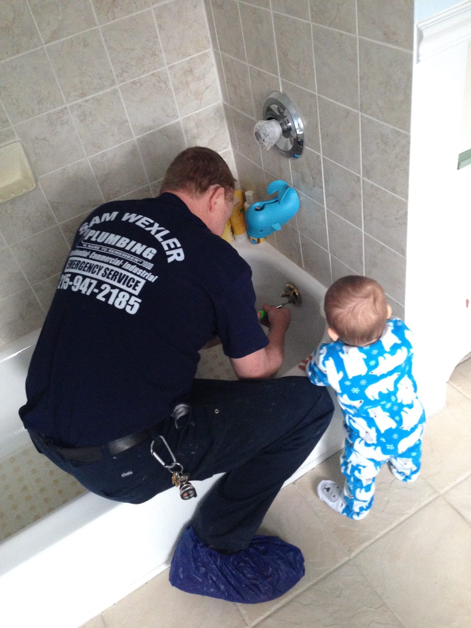 A plumber is working on a bathtub while a baby looks on.