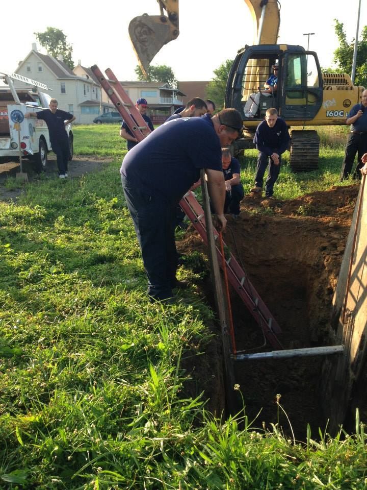 A group of men are digging a hole with a yellow excavator in the background
