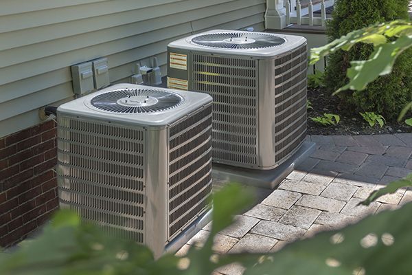 Two air conditioners are sitting on the side of a house.