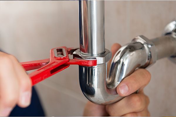 A plumber is fixing a pipe with a wrench.