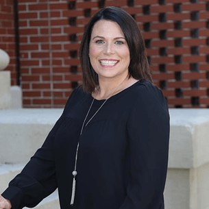 Smiling woman in a black top standing outdoors in front of a brick wall
