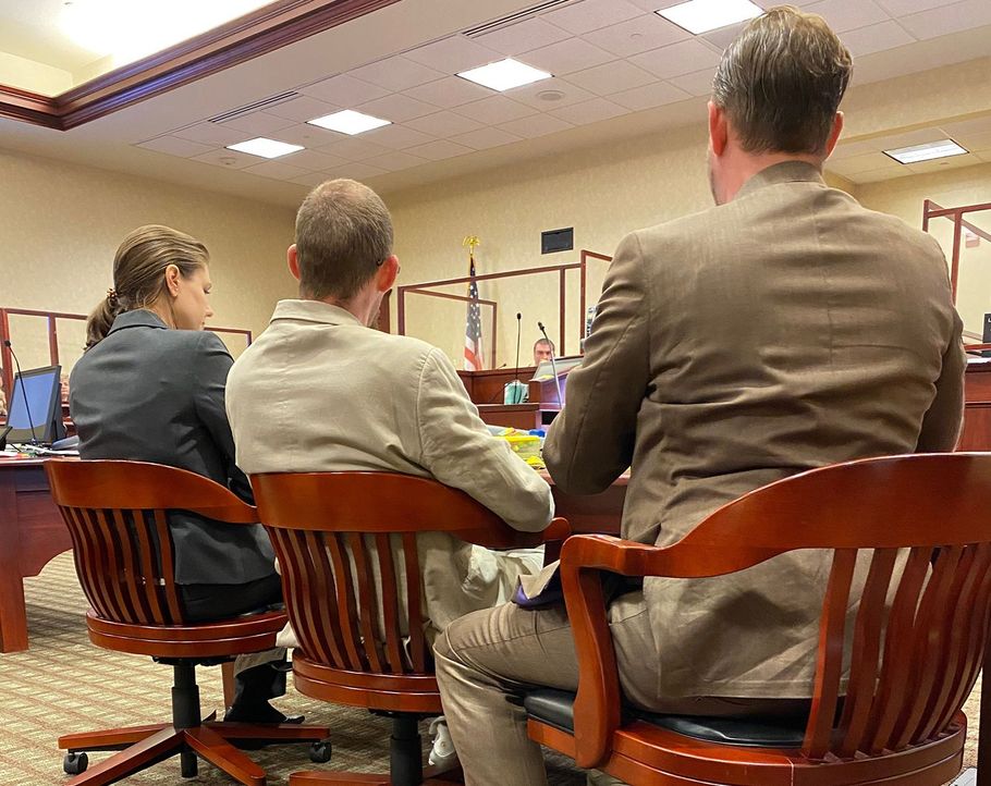 People seated in a courtroom, viewed from behind during a proceeding.