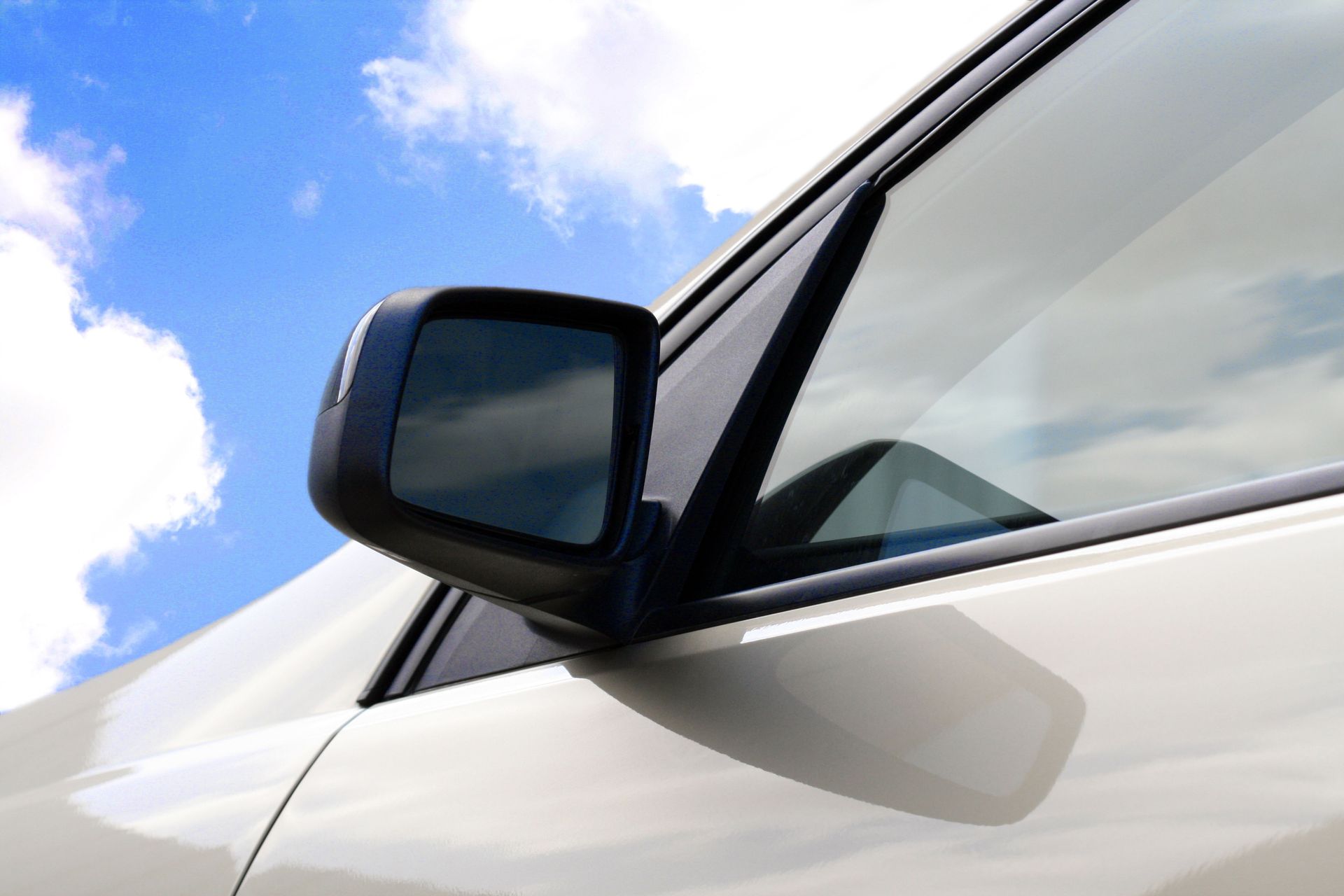 Close-up of a white car door and side mirror against a blue sky with clouds