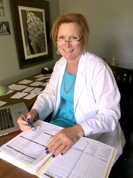 Julie Chicks, M.D., in a white coat reviewing documents at a desk with a laptop and papers