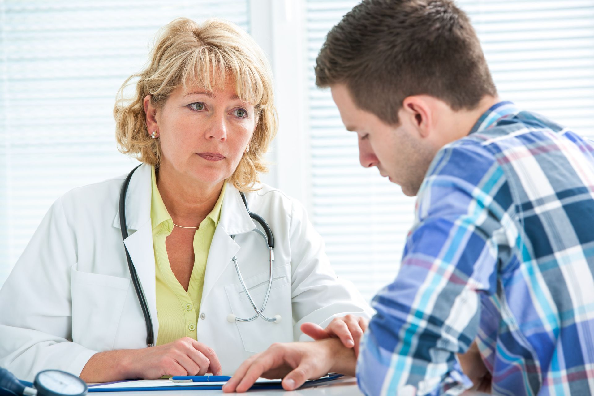 Doctor speaking with a patient at a desk in a bright clinic, reviewing paperwork together.