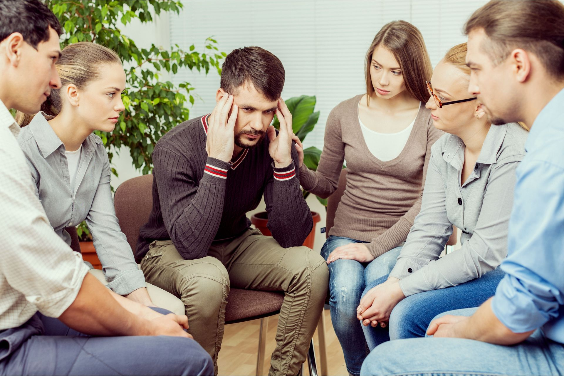 Group of people sitting in a circle, listening to a distressed man holding his head during a support meeting