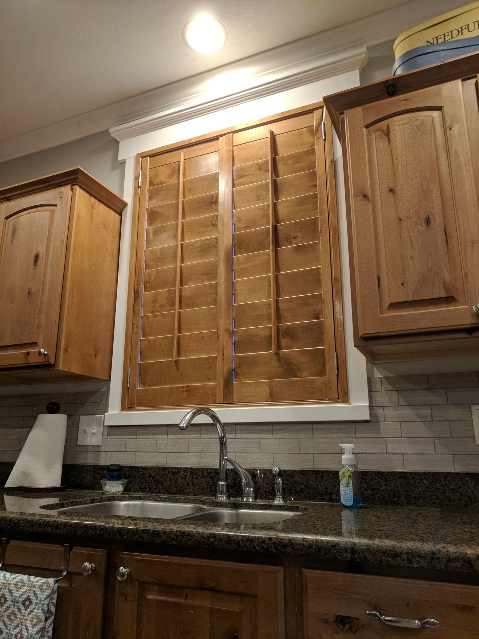 Kitchen with wooden cabinets, a sink, and window with wood shutters.