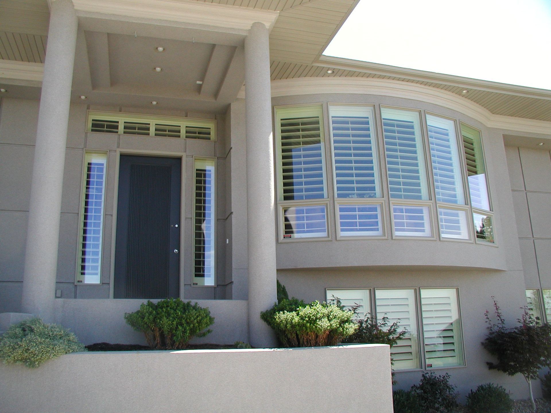 Exterior of a beige house with a dark door, arched windows, and shutters.