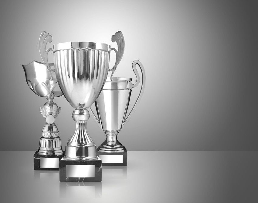 Silver trophies on a reflective surface with a gray gradient background.