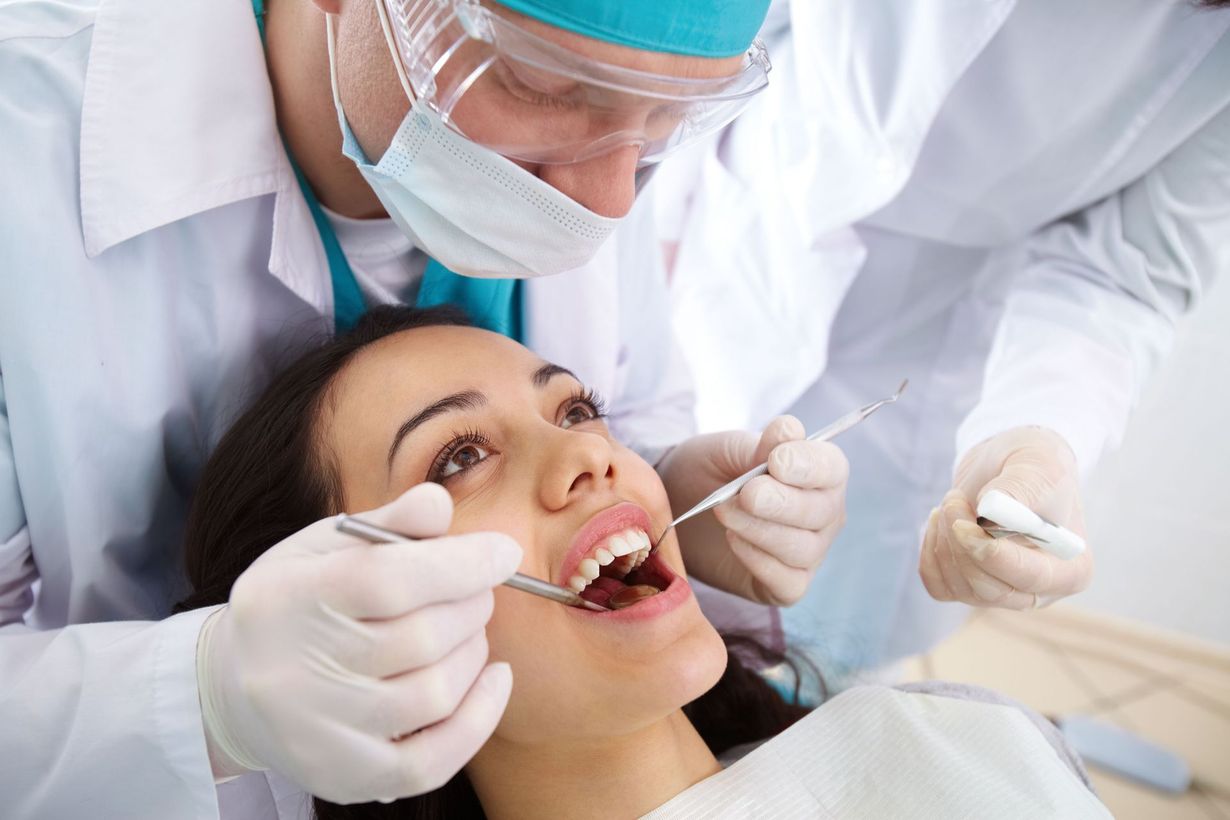Dentist examining a patient's teeth with tools. Patient in dental chair, mouth open.
